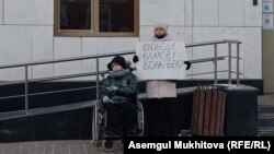 Акмарал Блялова, жена активиста Болатбека Блялова, арестованного на 15 суток, с плакатом стоит вместе с дочерью перед зданием Генеральной прокуратуры. Нур-Султан, 13 декабря 2021 года