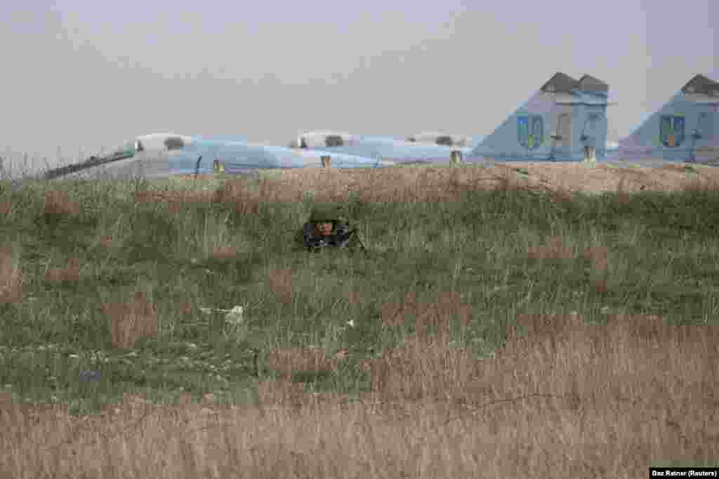 Российский военный наблюдает за украинскими военнослужащими в аэропорту Бельбек под Севастополем. База ВВС Украины стала одним из последних украинских оплотов в Крыму. Её командир отказался передать её российским войскам. В конце концов его задержали российские военные, а украинский персонал был выдворен