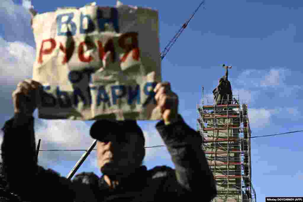 Мужчина держит плакат с надписью "Вон Россию из Болгарии", в то время как рабочие готовят леса вокруг памятника Советской армии перед его демонтажем в Софии.