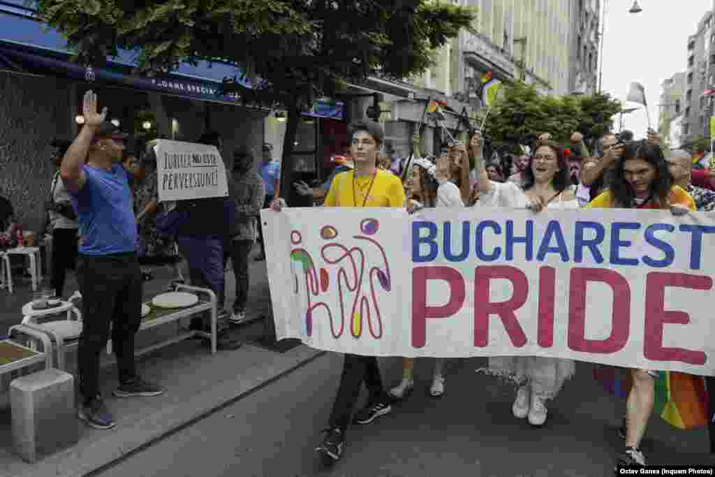 Participanții la parada Bucharest Pride 2023 trec pe lângă o persoană care poartă o pancartă cu mesajul „Iubirea nu este perversiune”.
