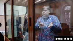 Aleksandra Bayazitova and Olga Arkharova stand in a defendants' cage while attending a court hearing in Moscow.