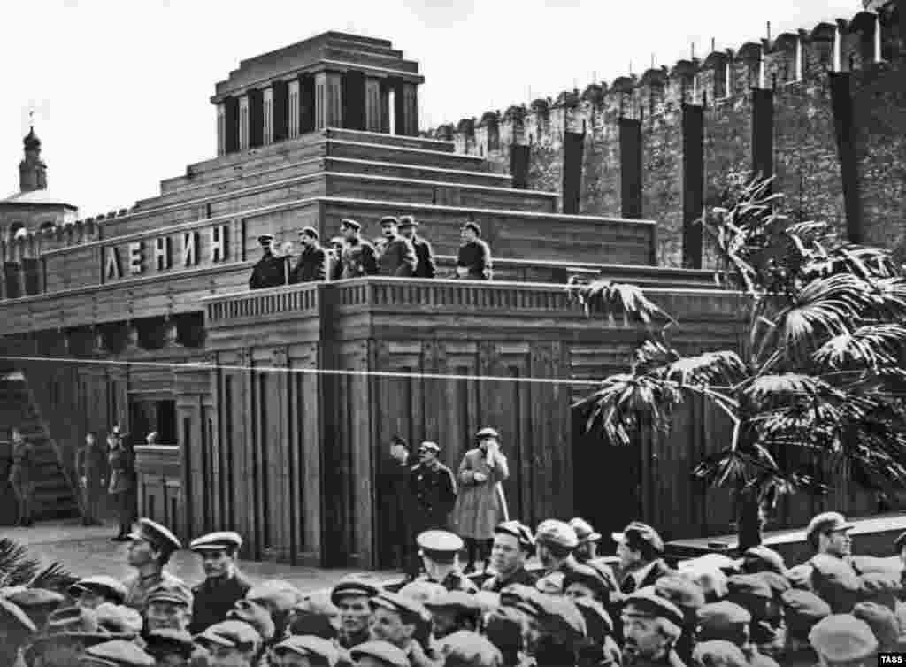 Liderii bolșevici, inclusiv Iosif Stalin (al treilea din dreapta, privind spre cameră), pe platforma oficială a celui de-al doilea mausoleu, în 1926. În martie 1924, acest mausoleu din lemn, de mai mari dimensiuni, a fost construit tot de Șciusev. Primul proiect întâmpinase mai multe dificultăți. Fiind mai mic, capriciile vremii și căldura generată de fluxul continuu de oameni care se perindau pe acolo riscau să ducă la putrezirea rămășițele lui Lenin.