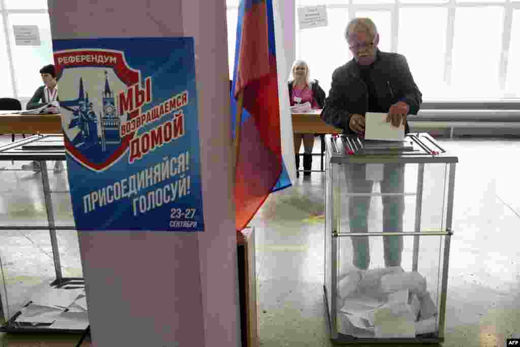 Egy férfi leadja szavazatát a referendumon egy mariupoli szavazóhelyiségben 2022. szeptember 27-én. „Hazatérünk” – hirdeti a plakát