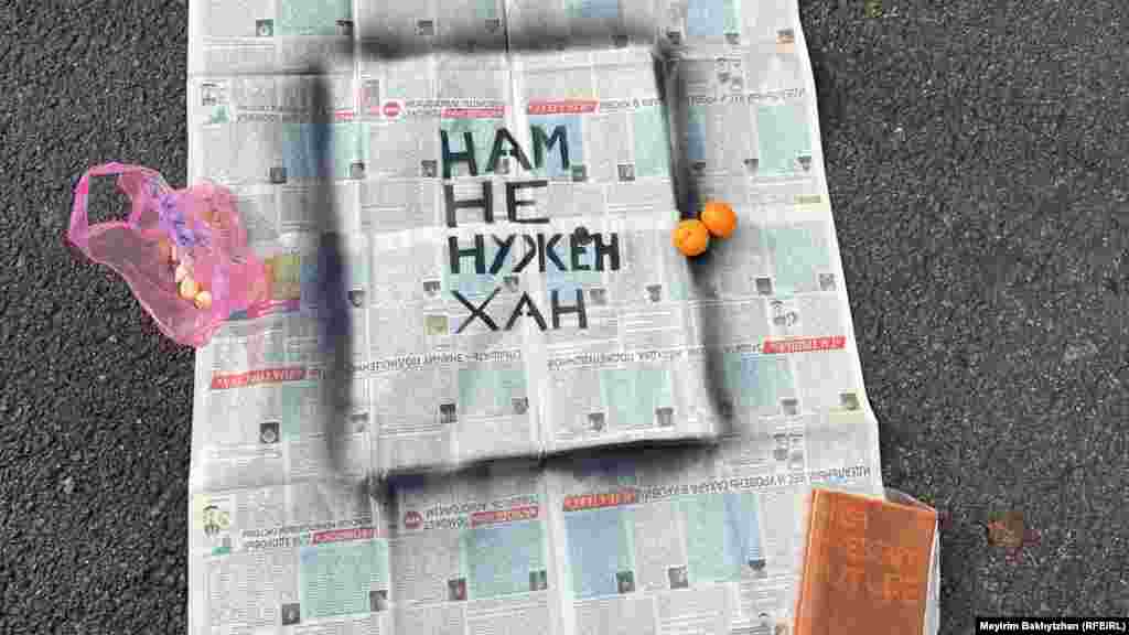 На митинге газета с надписью: «Нам не нужен хан» — лежит на земле. Уголок газеты придерживает предположительно ежедневник с надписью на обложке: Past, Present, Future (прошлое, настоящее, будущее — в переводе с английского)