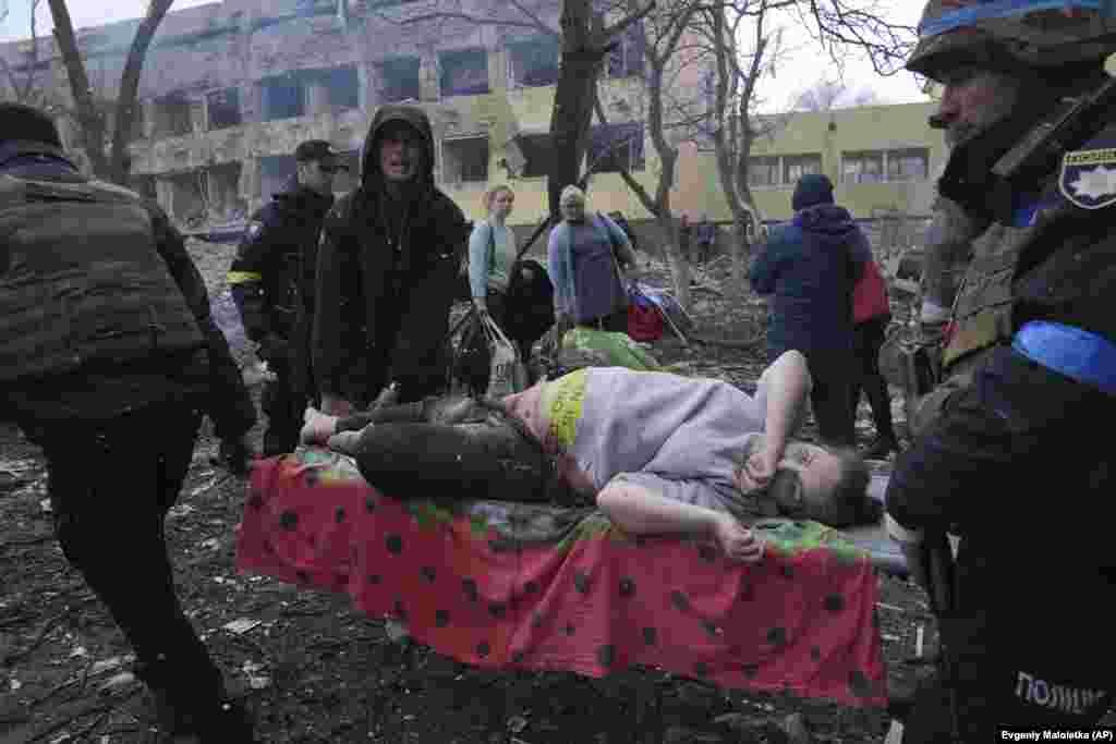 Украиналык куткаруучулар жана ыктыярчылар төрөт үйүнө орусиялыктар сокку ургандан кийин жаракат алган кош бойлуу аялды алып чыгып баратышат. Мариуполь, 9-март, 2022-жыл.