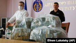 Klymenko's predecessor, Nazar Kholodnytskiy (left) leads a briefing next to $6 million in plastic bags in June 2020, two months before he resigned amid allegations that he helped officials suspected of corruption evade prosecution.