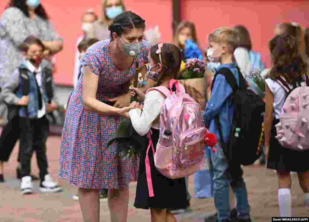 A woman and a girl wearing protective face masks chat as they gather with teachers, parents, and other children in front of a school in the Romanian capital, Bucharest, on September 14 as classes started again after the summer break. Due to the coronavirus pandemic, most of Romania's schools reopened with students alternating between classroom learning and remote education.