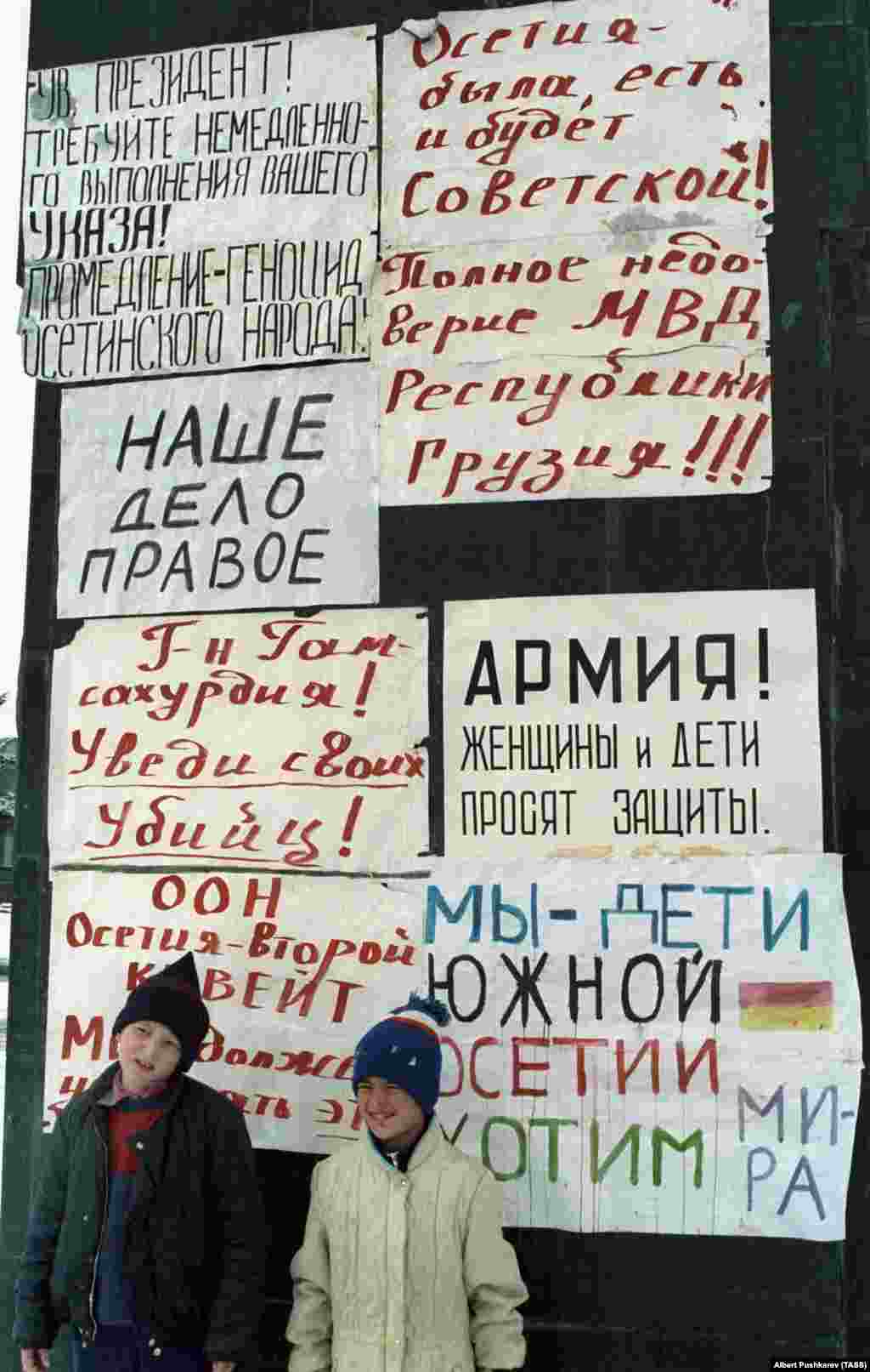 "Осетия советтік болған, бола береді де!" деген жазуы бар плакаттың астында тұрған балалар. 1 қаңтар 1991 жыл. Грузия Совет Одағынан бөлініп, тәуелсіз ел болуға талпынғанда көптеген грузин осетиндерден сескеніп, оларды "бесінші колонна" көрді. Ал осетиндер өздерін оқшауланғандай сезінді. Жаңа қабылданған заңдар грузин тілін мемлекеттік тіл етіп бекітіп, осетиндердің Тбилисидегі саяси өкілдігіне шектеу қойды.