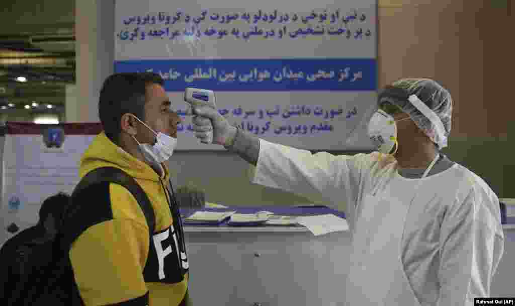 An Afghan health-care worker takes the temperature of a passenger during a screening process for travelers who had arrived in Kabul from China.