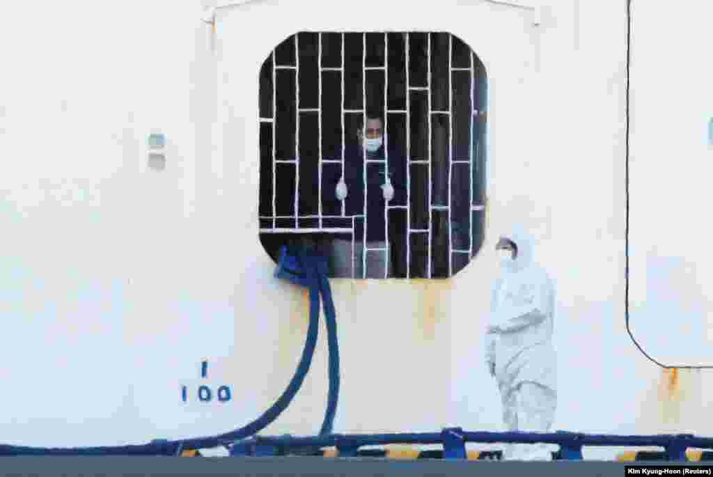 A crew member of the Diamond Princess talks to a worker in protective gear. Crew and passengers are now required to wear gloves and a face mask at all times when outside their cabins. 