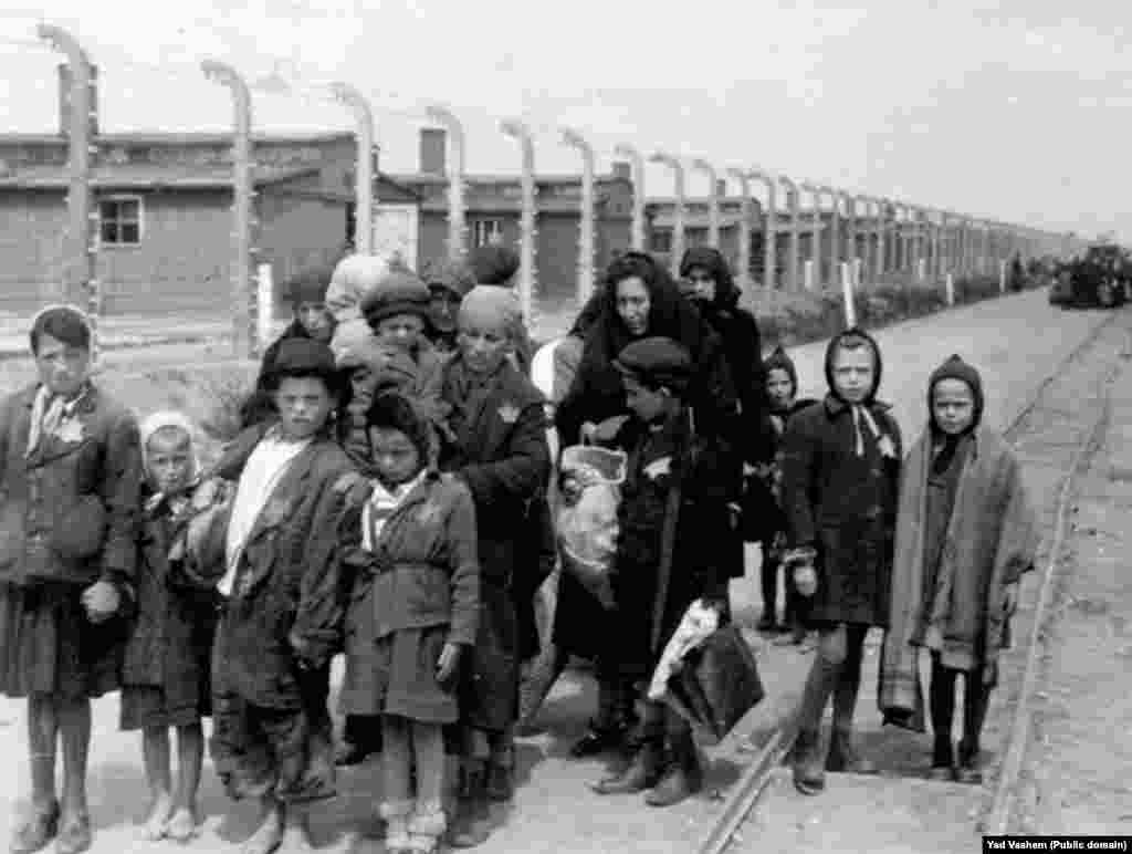 На фото справа: 1944 год. Женщина с детьми направляется в газовую камеру. На заднем фоне виднеются деревянные бараки – это лагеря «Биркенау», которые дополнительно были построены в «Освенциме». После войны эти здания были разрушены, но кирпичные стены и дымоходы сохранились