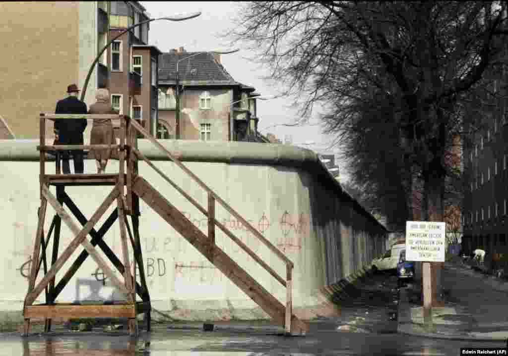 Пара смотрит через стену на Восточный Берлин, снимок сделан в апреле 1983 года. Герхард Зальтер говорит, что испытания противотранспортных заграждений были лишь только частью обширных испытаний и разработок, направленных на то, чтобы не допустить побега из полицейского государства. Сама конструкция Берлинской стены, по его словам, испытывалась "на устойчивость к нападениям с использованием транспортных средств, взрывчатых веществ, а также на выносливость в случае природных катастроф, например, в случае мощных потоков воды во время сильных дождей".