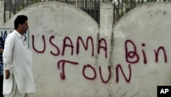 Pakistanly adam “Osama Bin Şäherçesi” diýlip, üstüne ýazgy ýazylan diwaryň deňinden geçip barýar, Abbottabat, 2011-nji ýylyň 6-njy maýy.