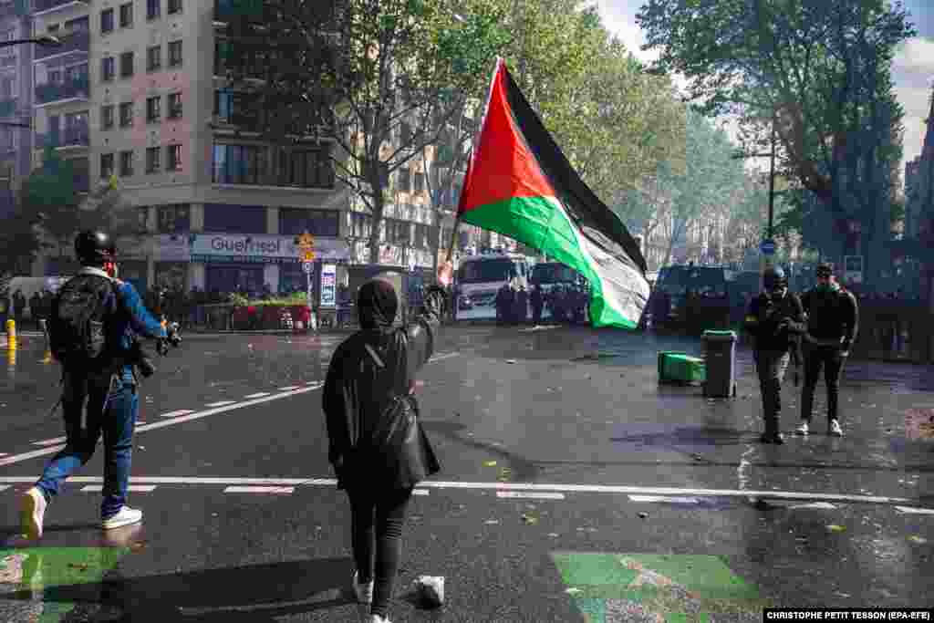 Një grua valëvit një flamur palestinez, teksa protestuesit përballen me policinë kundër trazirave, gjatë përleshjeve si pjesë e një tubimi të organizuar nga disa shoqata, në mbështetje të popullit palestinez, në Paris, Francë, më 15 maj 2021.