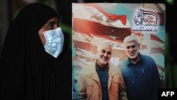 An Iraqi woman in Baghdad carries a portrait of Iranian Major General Qasem Soleimani (left) and Iraqi militiaman Abu Mahdi al-Mohandes at an event to mark the first anniversary of their death in a U.S. air strike.
