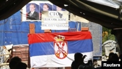 People sit in the tent on a road blockade decorated with the Serbian flag and pictures of Russian Prime Minister Vladimir Putin in the village of Rudare, near Mitrovica on August 7, 2011.