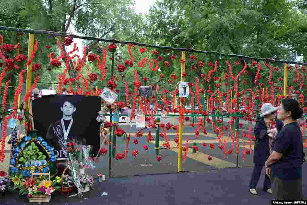 19 июля 2018 года Денис Тен пытался задержать воров, которые хотели снять зеркала с его автомобиля, и получил от одного из преступников ножевое ранение. Оно оказалось смертельным. Через несколько часов спортсмен умер в больнице. Ему было 25 лет. Рядом с местом его гибели почти сразу же образовалась стена памяти — большой фотопортрет на сетке, которой огорожена спортплощадка. Рядом — его фотографии поменьше. Люди несли сюда цветы и игрушки. Казахстан, Алматы, 22 июня 2019 года.