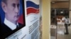 RUSSIA -- A man wearing a protective face mask and gloves prepares to cast his ballot during early voting in a referendum on amendments to the Russian Constitution next to a portrait of Russian President Vladimir Putin at a polling station in Moscow, June