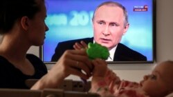 A Russian woman plays with her baby while watching the televised call-in show with President Vladimir Putin in Moscow.